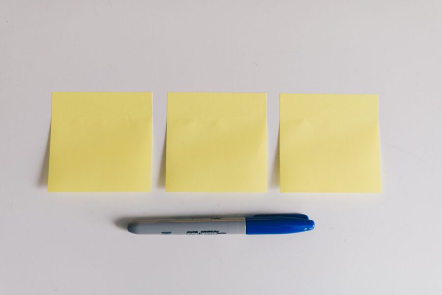 Three blank yellow sticky notes and a blue marker on a white desk