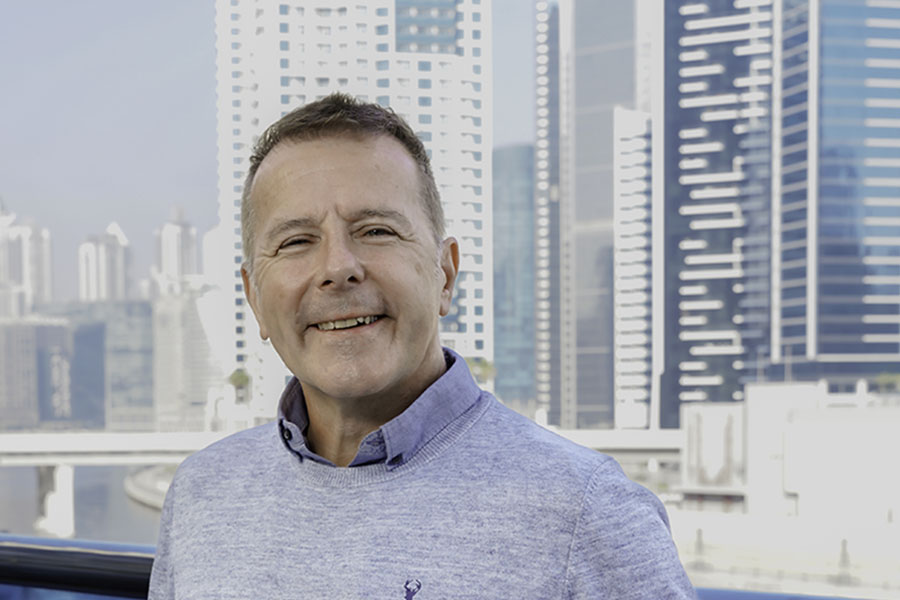 Smiling man in a light blue jumper in front of a city skyline