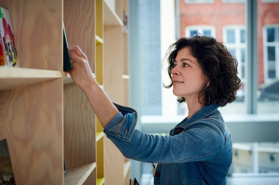 Woman taking a book from a wooden shelf