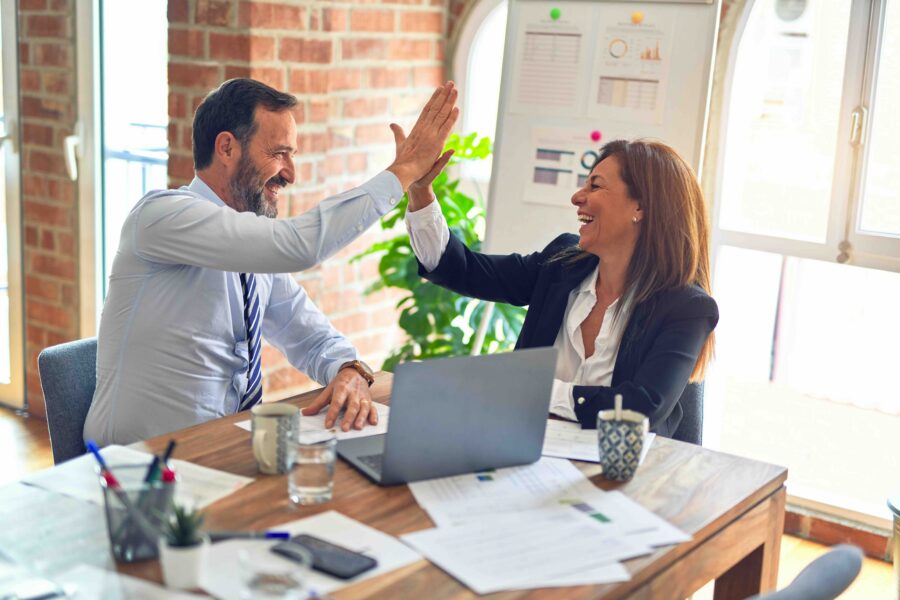 Two colleagues high-fiving across a desk in a bright office