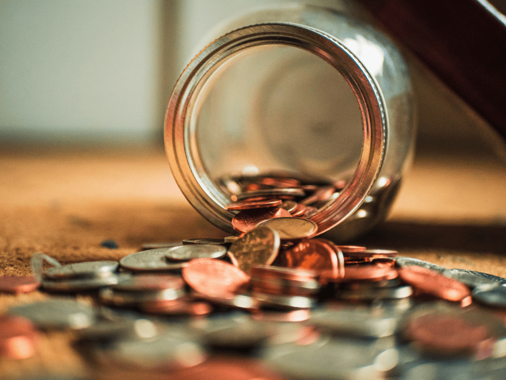 Jar of coins tipped over with coins spilling onto a table
