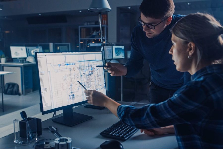 Two engineers reviewing technical drawings on a large monitor