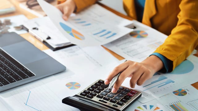 Person using a calculator over financial charts and reports